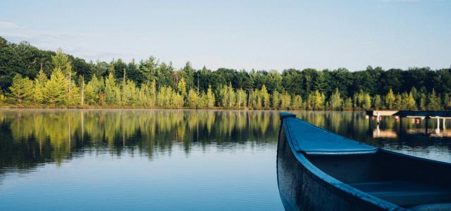 grey canoe on calm body of water near tall trees at daytime by Aaron Burden courtesy of Unsplash.